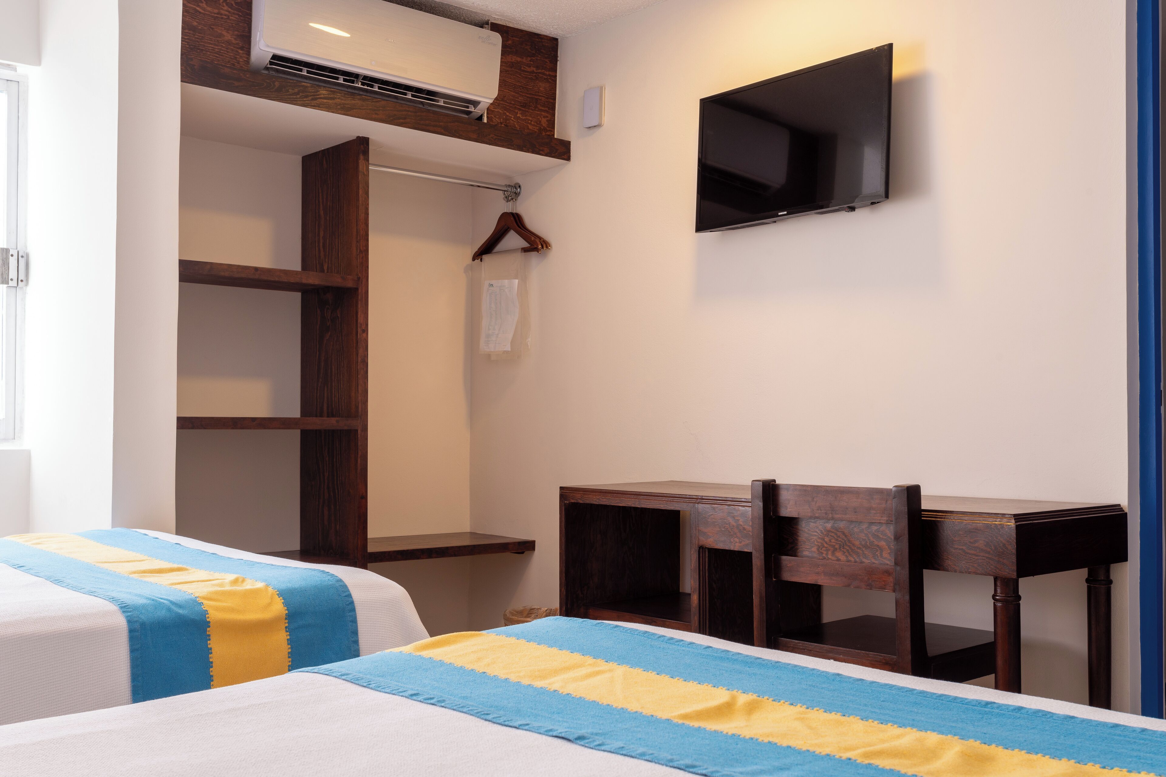 Habitación de hotel con dos camas, un televisor montado en la pared, un escritorio de madera y un armario.