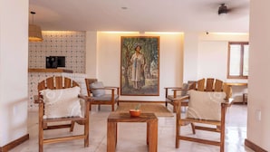 Uma sala de estar com cadeiras de madeira, uma mesa de centro e um quadro na parede.
