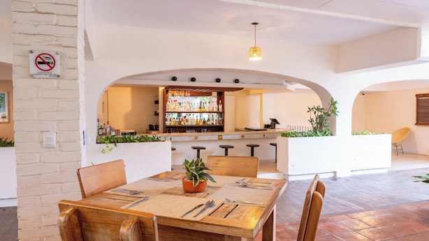 A dining area with a wooden table, chairs, and a bar in the background.