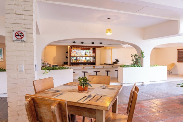 Un comedor con mesa de madera, sillas y barra al fondo.