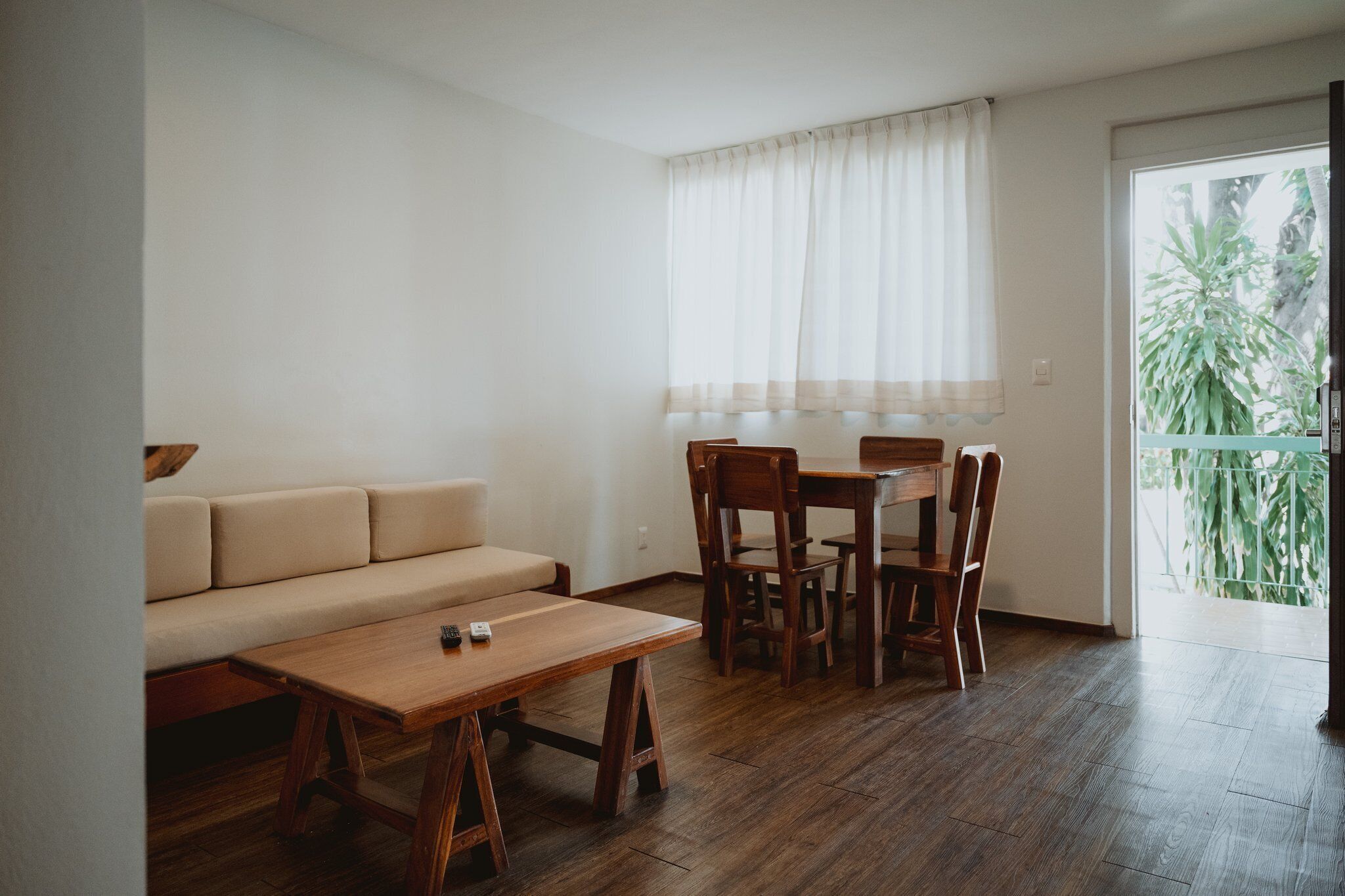 Une pièce comprenant un canapé, une table à manger en bois, des chaises et une fenêtre avec des rideaux.