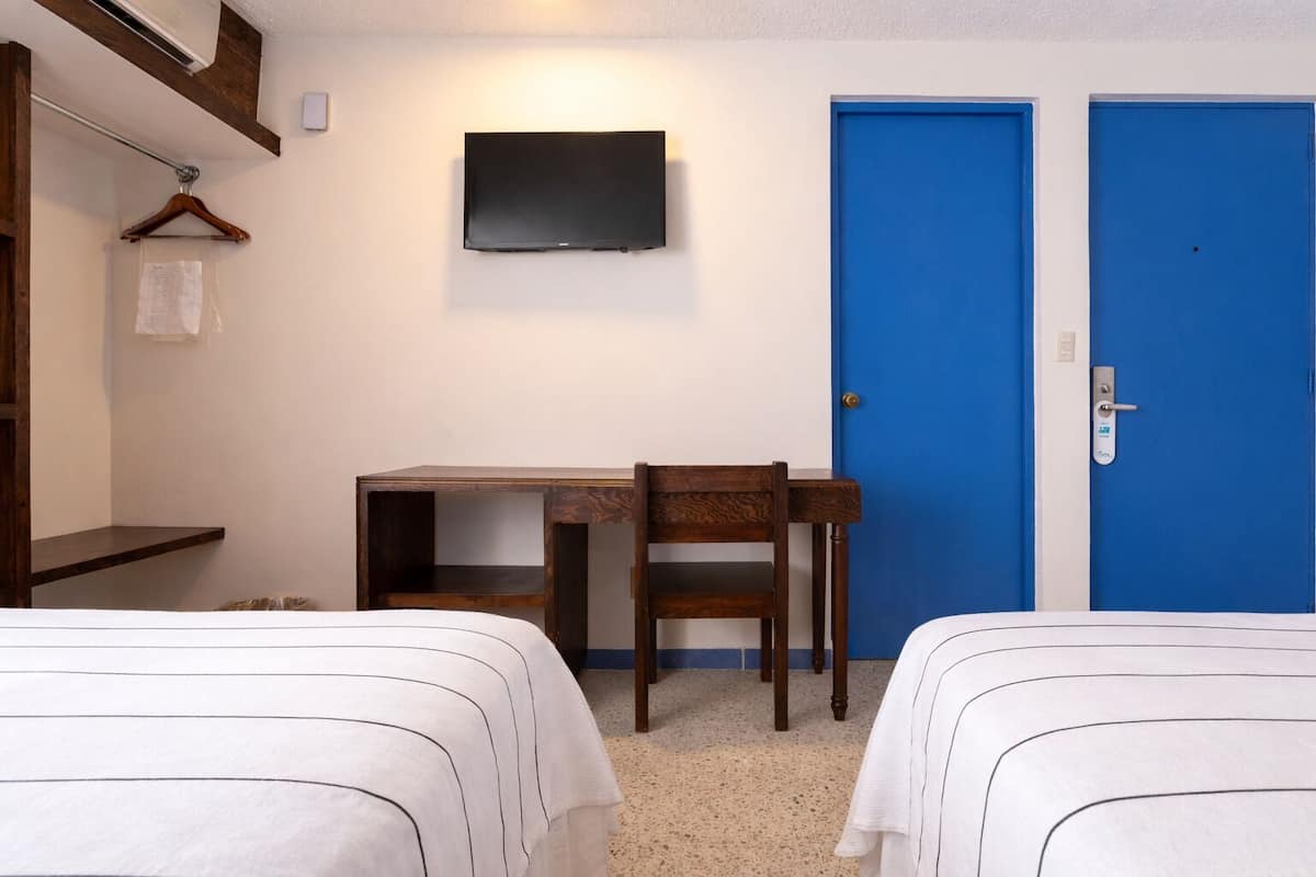 Hotellihuone, jossa on kaksi sänkyä, työpöytä, tuoli, televisio ja sininen ovi.