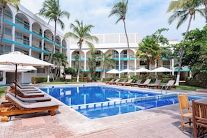 A swimming pool area with lounge chairs and umbrellas, surrounded by a multi-story building with balconies.