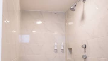 Un baño moderno con baldosas de mármol, cabezal de ducha y dos dispensadores de jabón para manos.