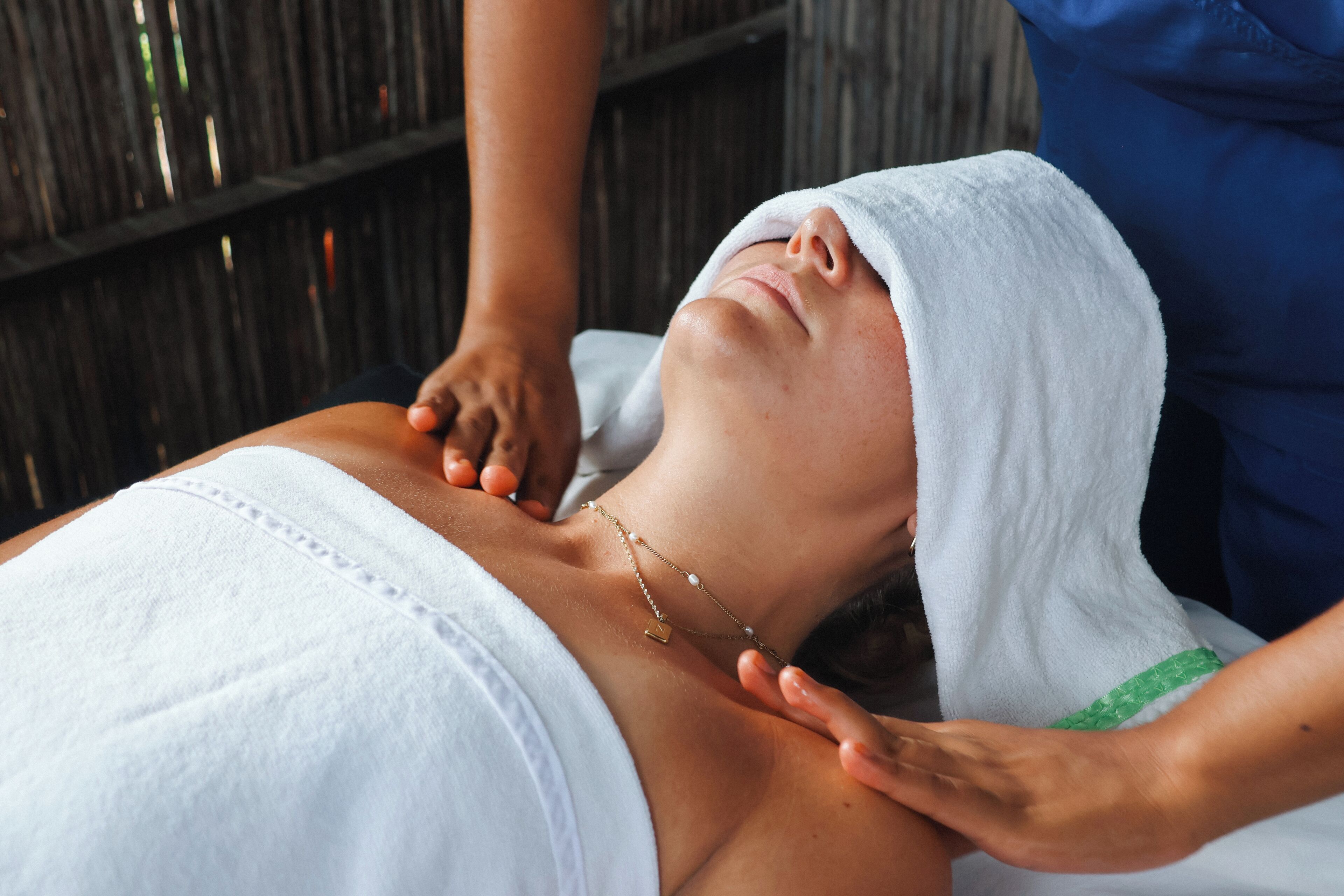 A person receiving a massage with a towel over their head, a necklace, and a wooden background.