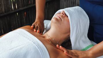 A person receiving a massage with a towel over their head, a necklace, and a wooden background.
