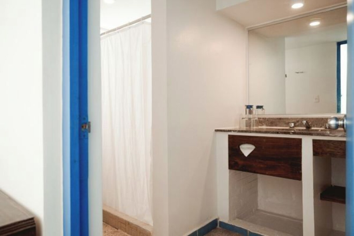 Un baño con pared blanca, marco de puerta azul, espejo, lavabo y toallero.