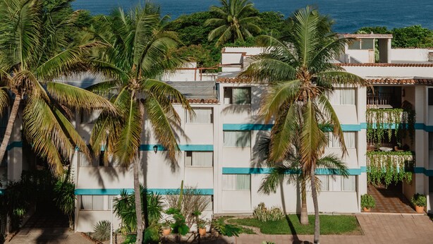 Um hotel à beira-mar com edifícios de vários andares, palmeiras e vista para o oceano.