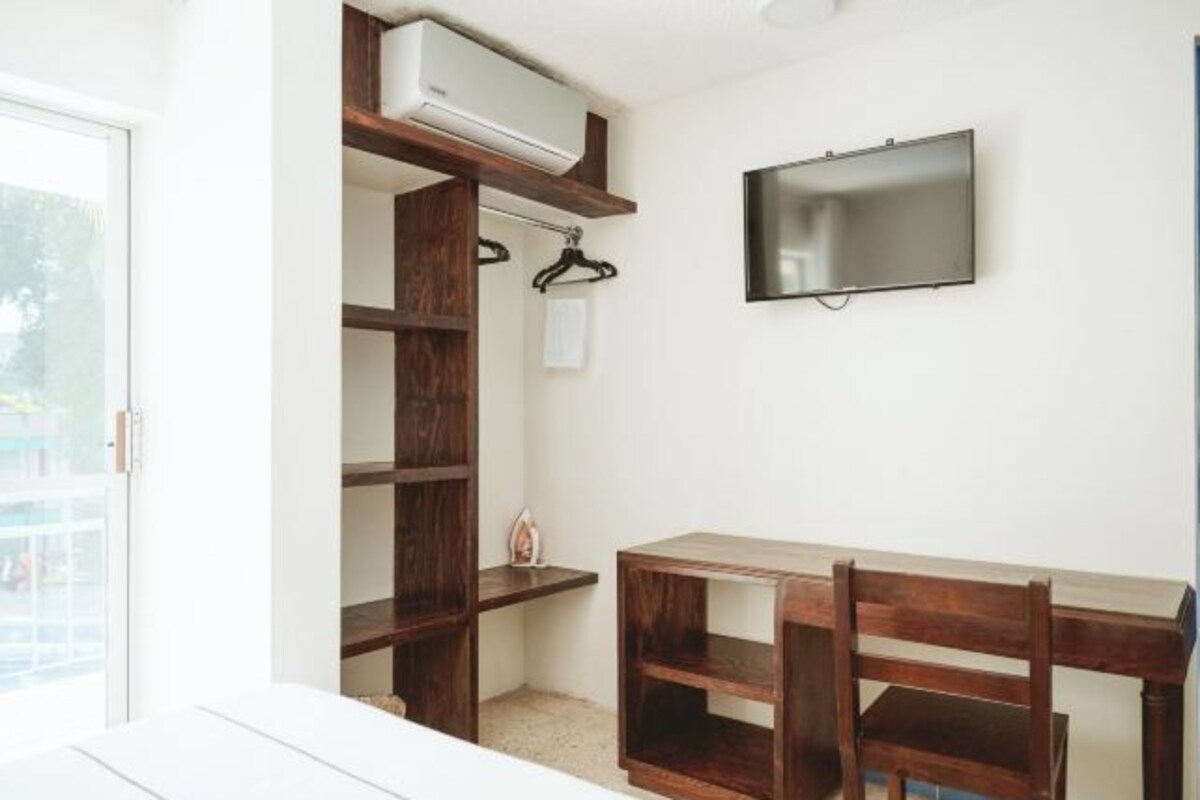 Una habitación con un escritorio de madera, una silla, un televisor montado en la pared y un armario empotrado de madera.