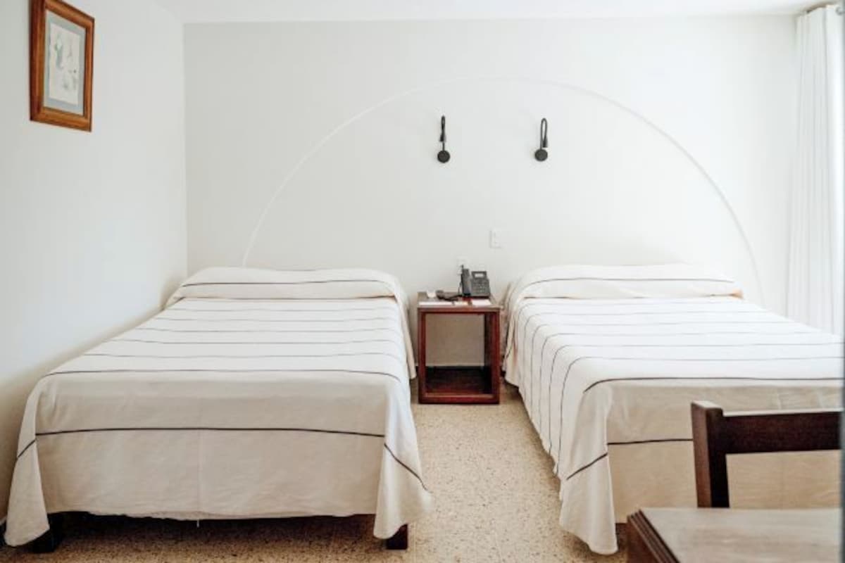 A room with two beds, a small table, and a nightstand with a lamp.