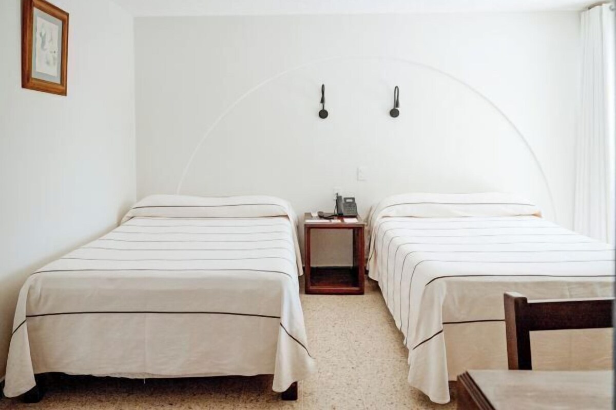 Una habitación con dos camas, una mesita y una mesita de noche con lámpara.