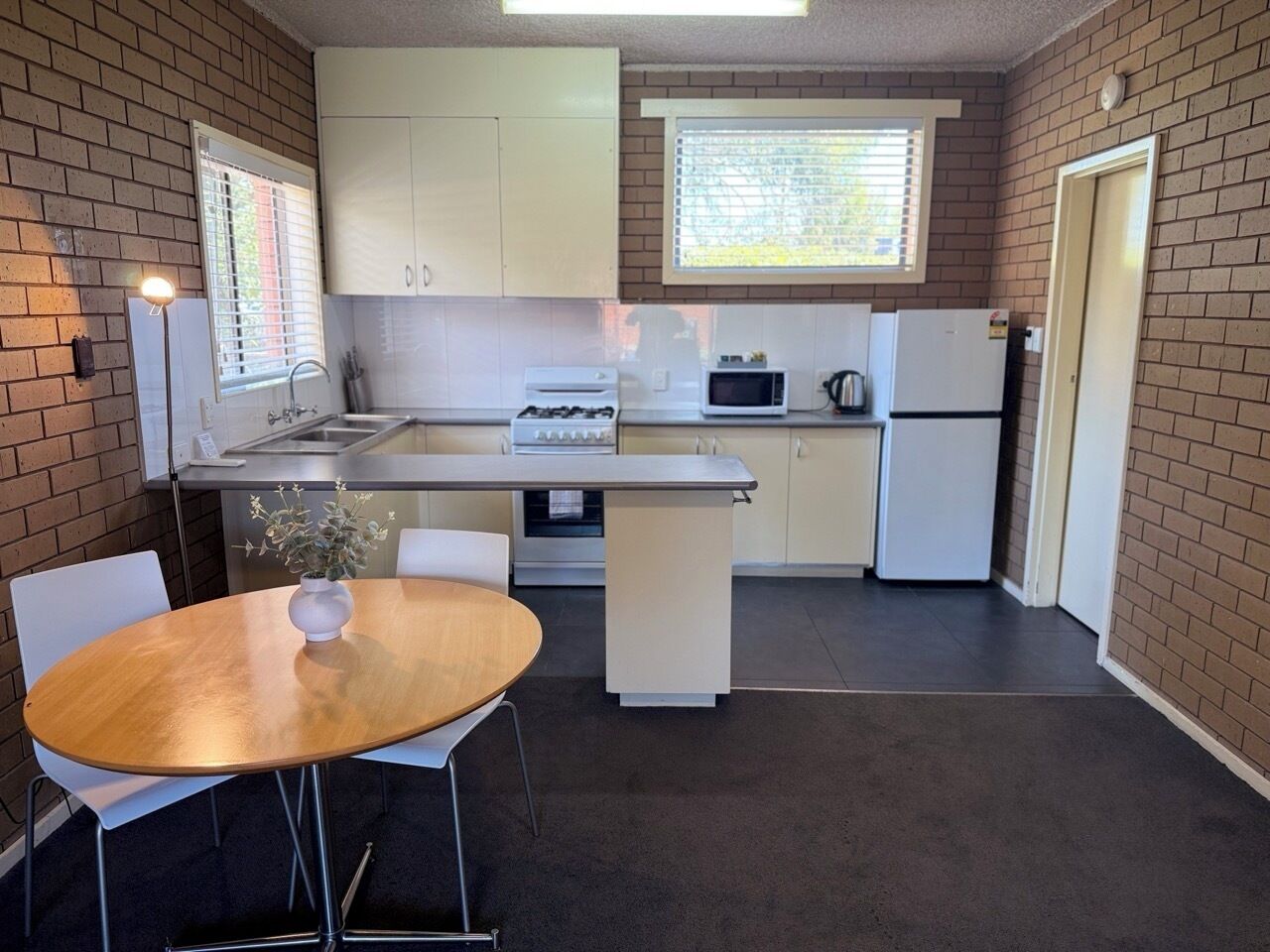 A compact kitchen with white cabinets, a stove, a microwave, and a refrigerator. There is a small island with a sink and a dining table with chairs.