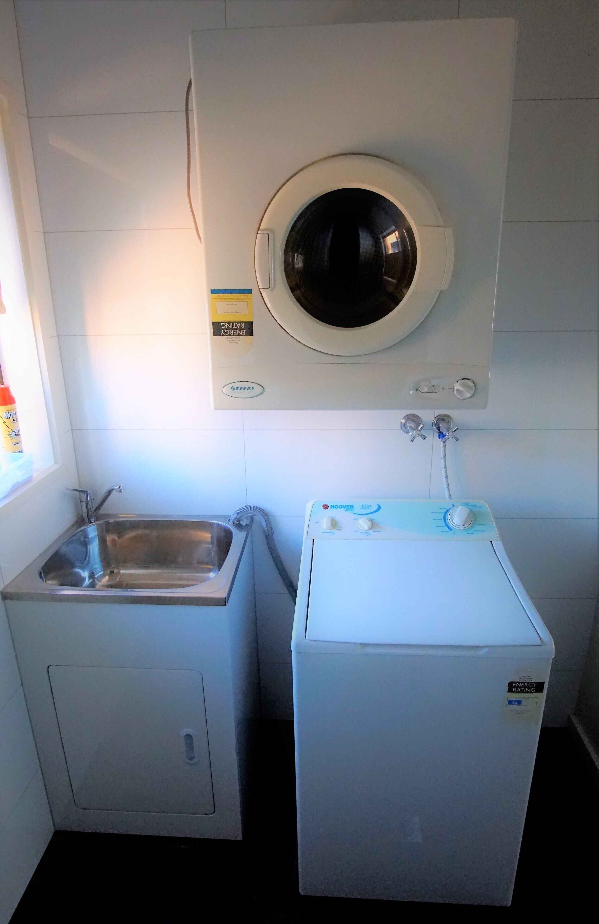 A compact laundry area with a built-in washer and dryer, a small sink, and a window providing natural light.