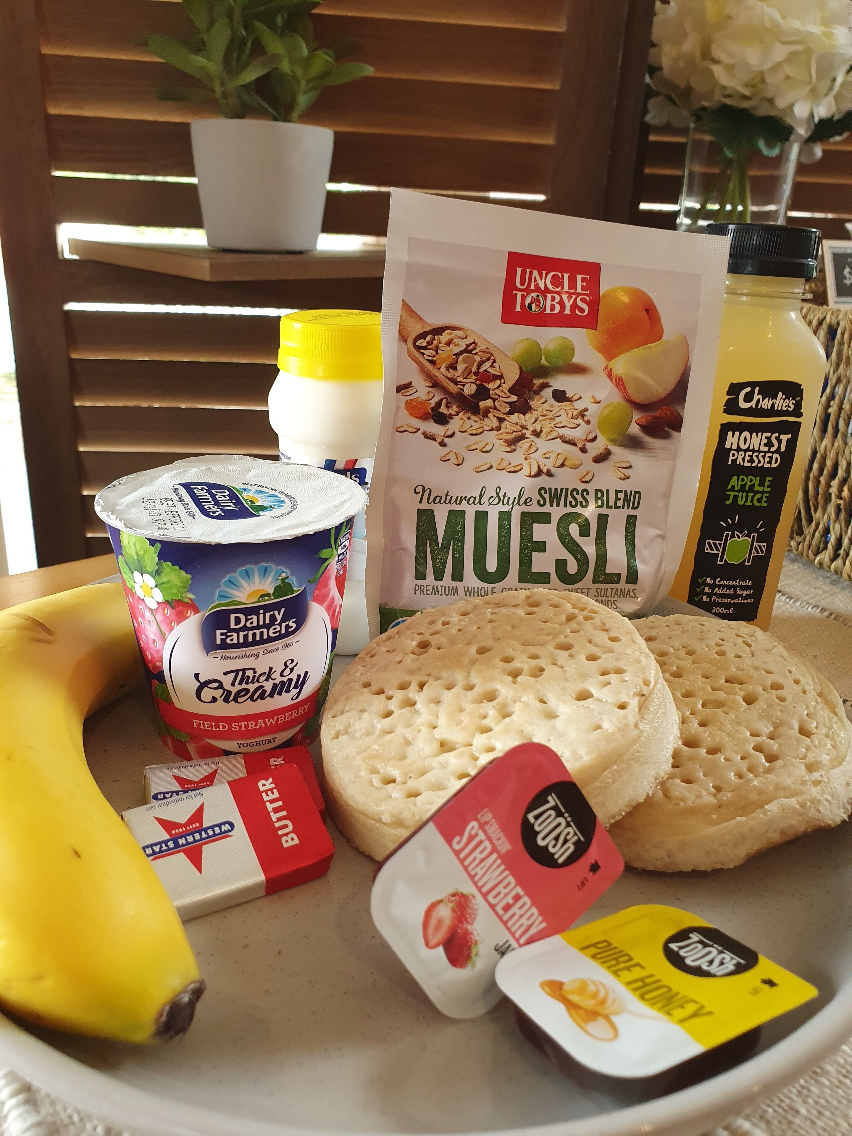 Un plat amb aliments com iogurt, muesli, un plàtan, galetes i una ampolla de suc.