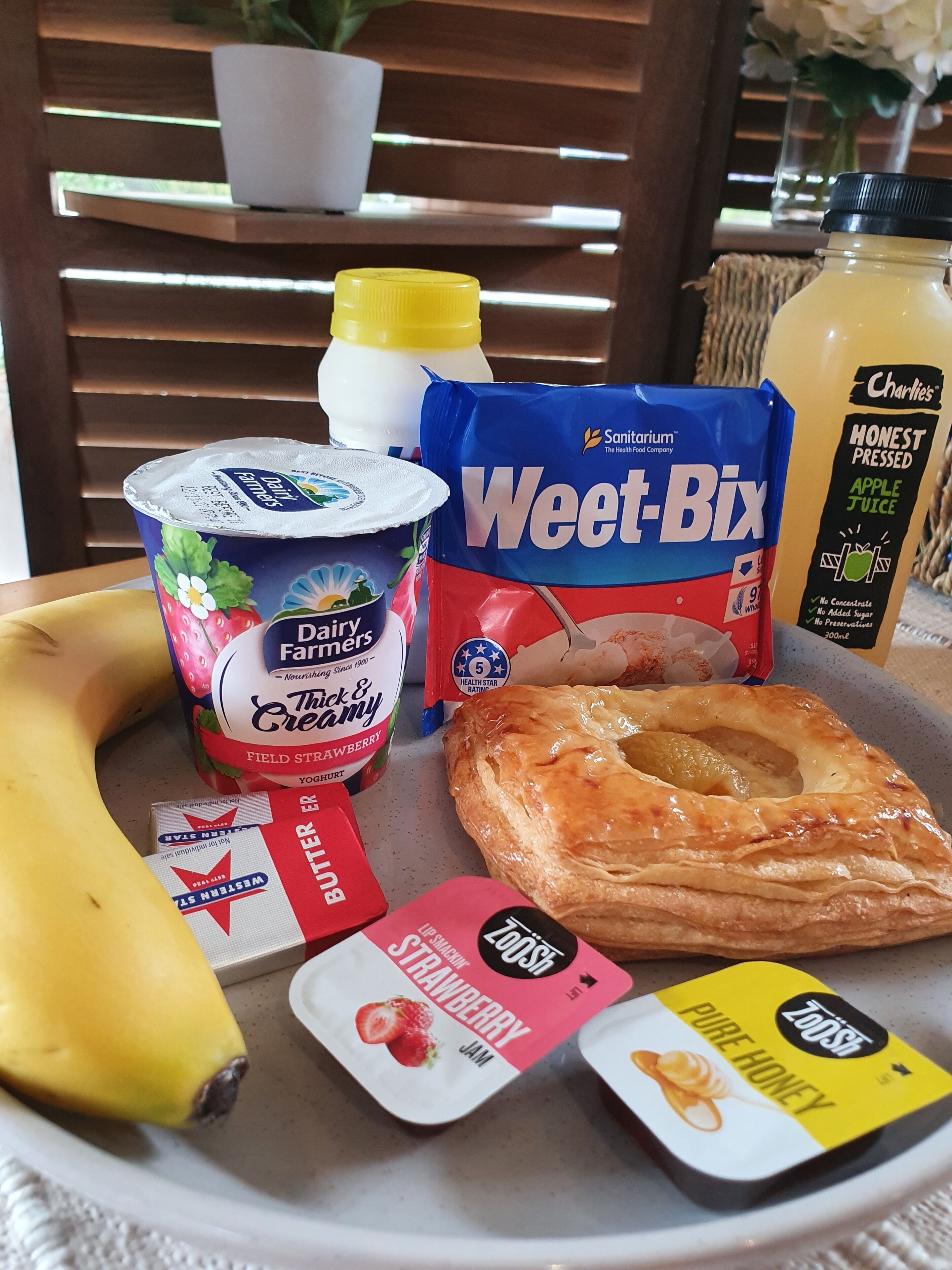 Un vassoio con cibi tra cui una banana, un dolce, yogurt, una bottiglia di succo e snack confezionati.