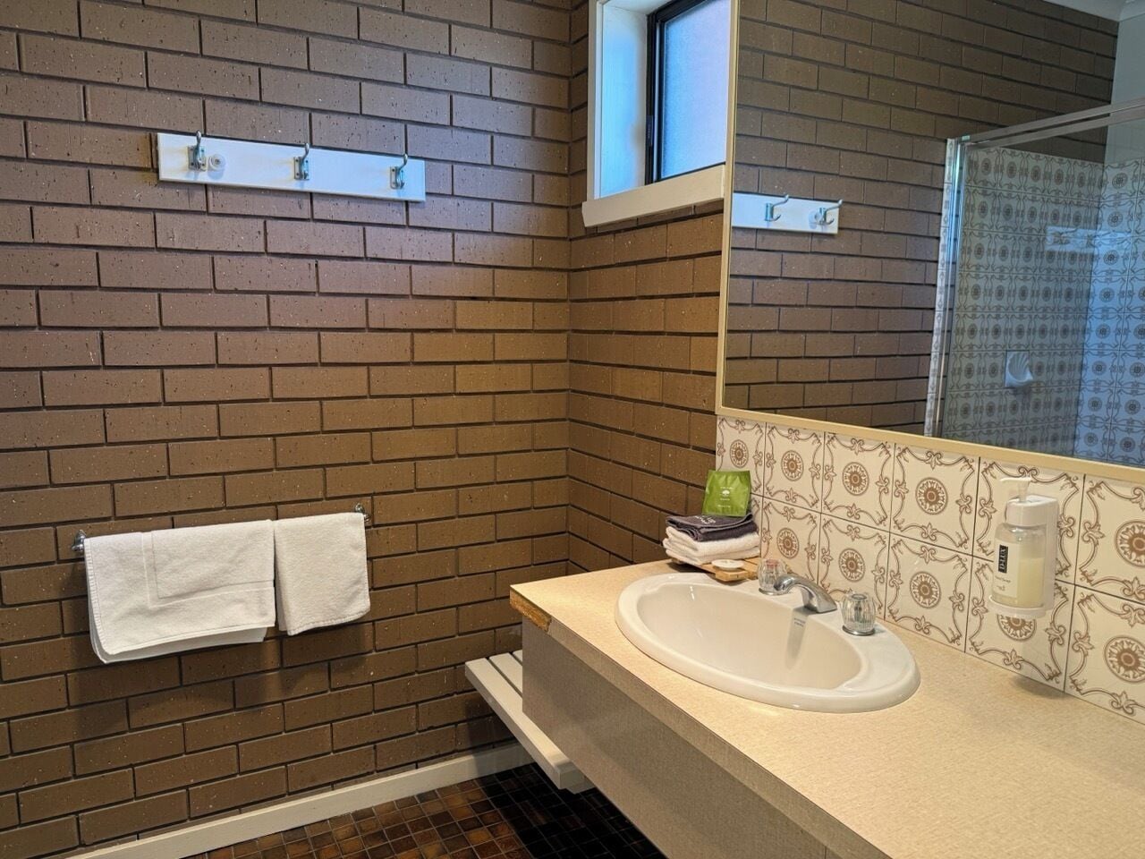 A bathroom with a brick wall, a white sink, and a mirror.