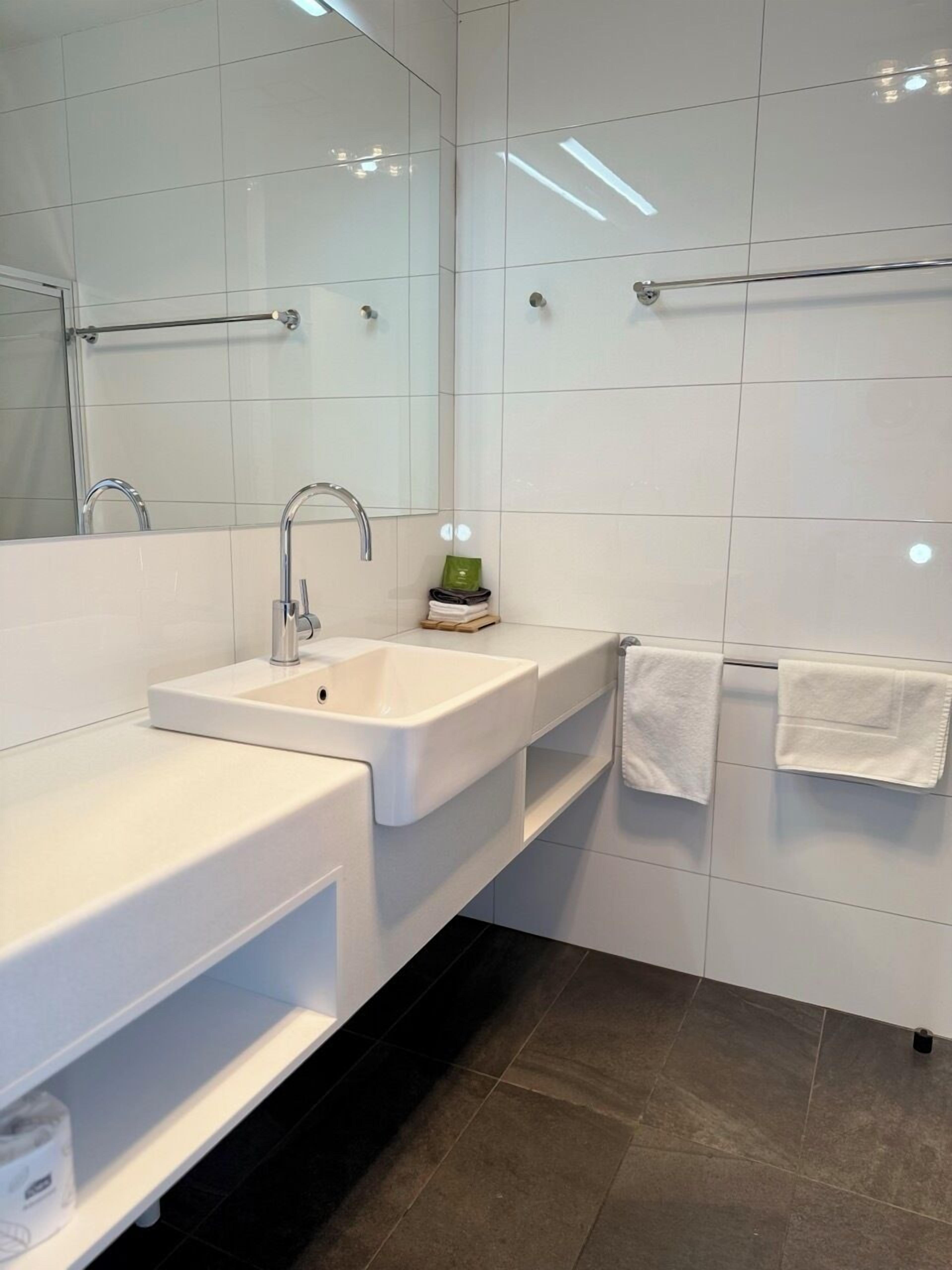 A modern bathroom with a white sink, mirror, and towel rack.