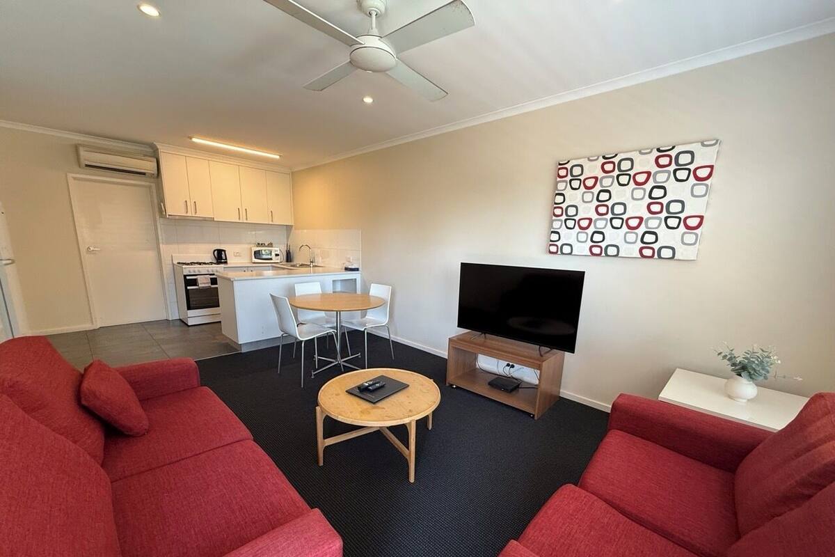 A compact living space with a kitchenette, a dining area, and a seating area with red sofas and a coffee table.
