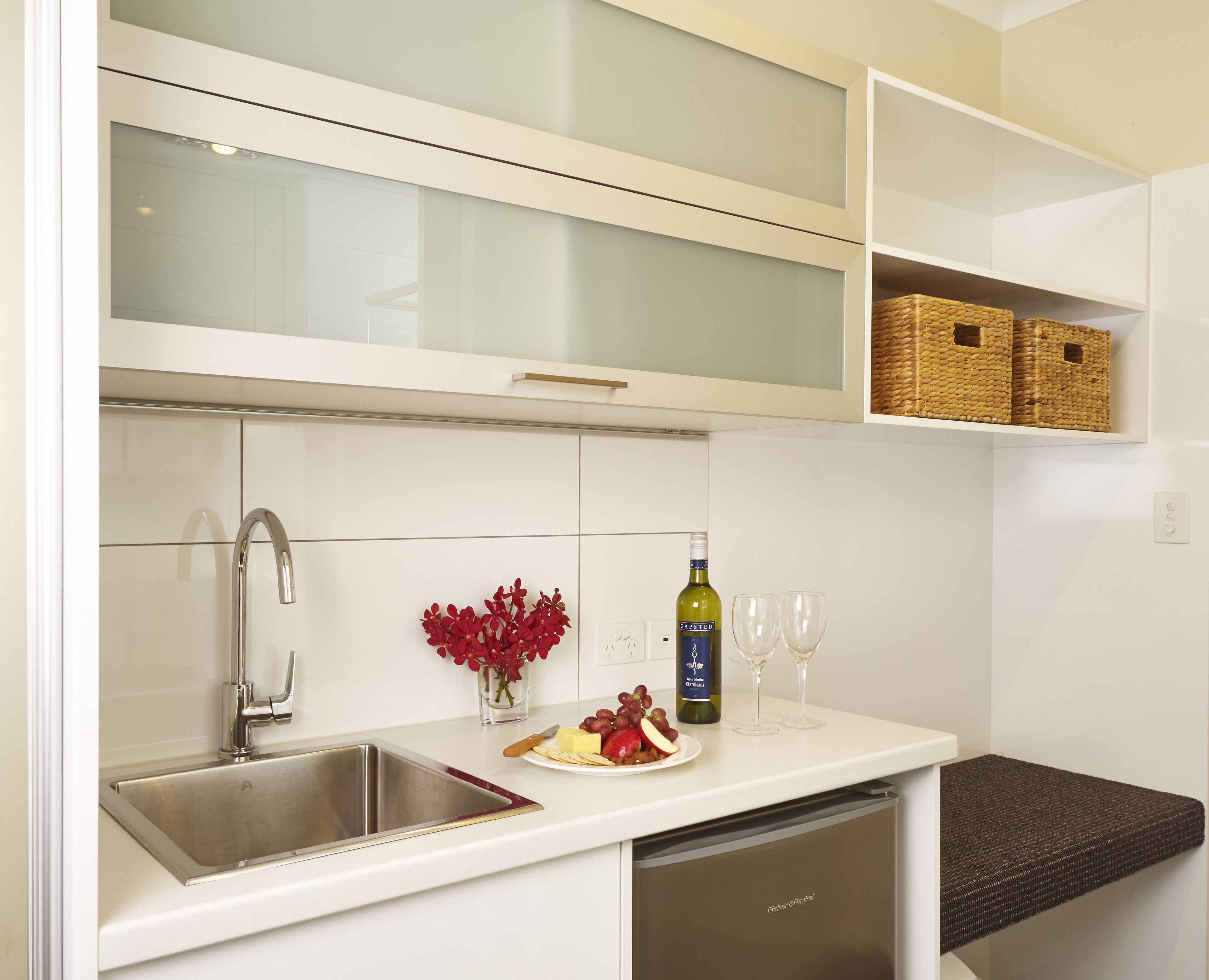 Una cocina moderna con un lavamanos de acero inoxidable, una botella de vino y una copa de vino sobre la encimera.