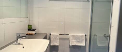 A modern bathroom with a sink, two towels, and a glass shower enclosure.