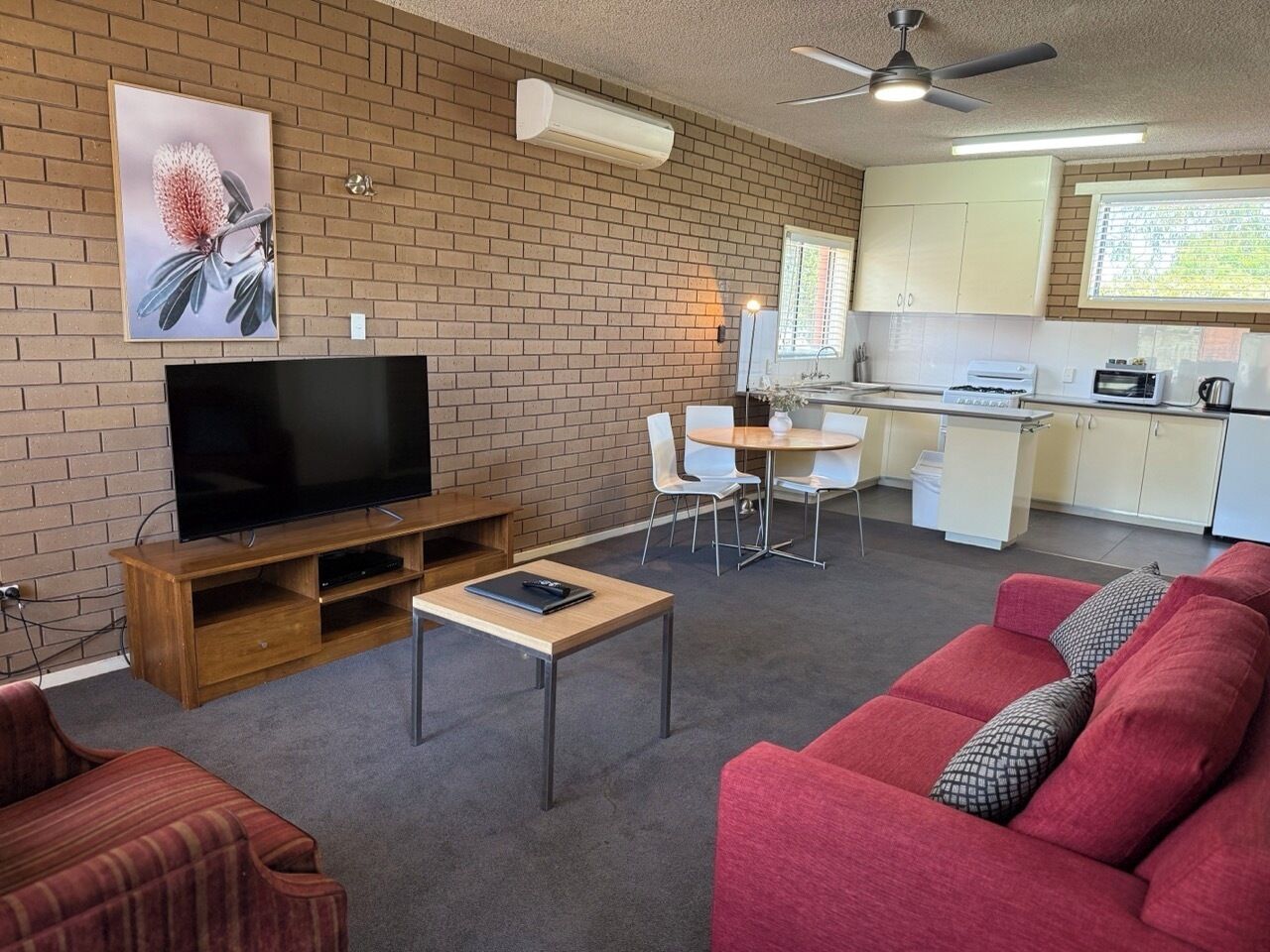 Ein Wohnzimmer mit Fernseher, einem roten Sofa, einem Holztisch und einer Küche im Hintergrund.