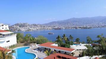 A resort with a swimming pool, palm trees, and a view of a city and mountains.
