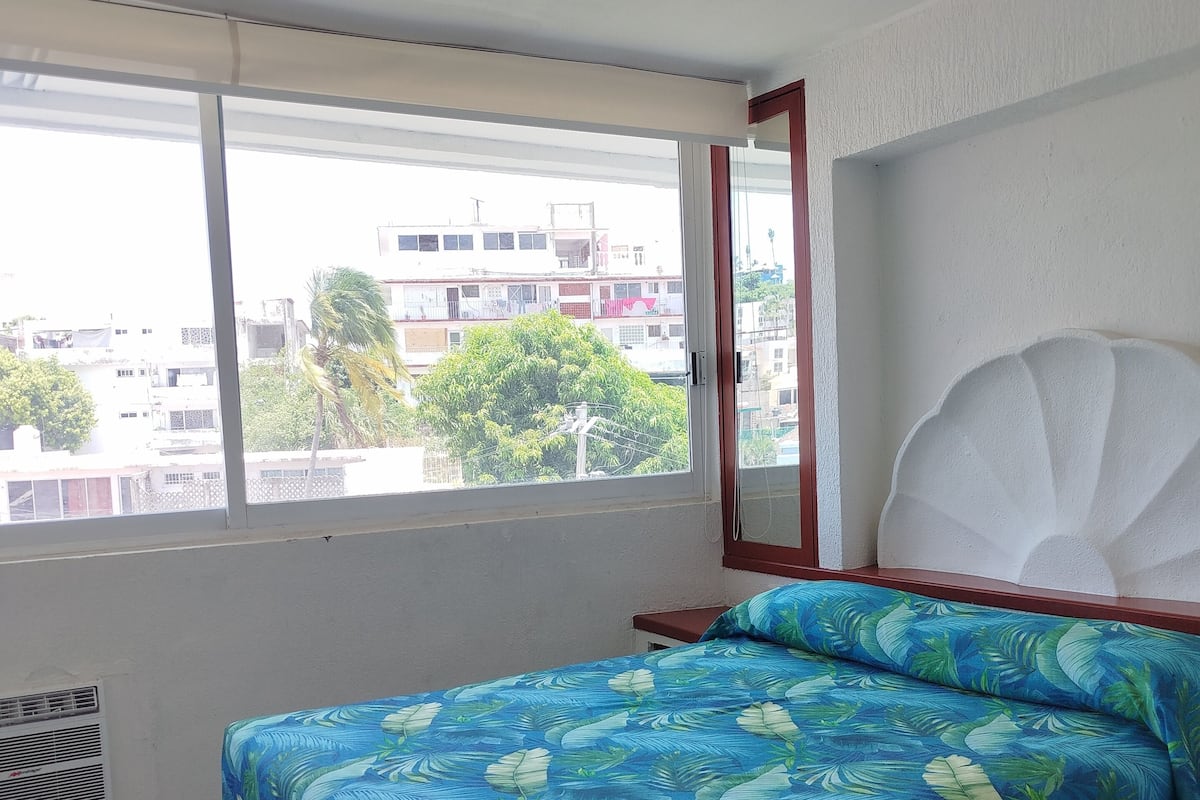 Una habitación con cama, ventana y vistas a edificios.