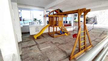Kids can play and climb on the slide and structure, taking in the view of palm trees and the surrounding building.