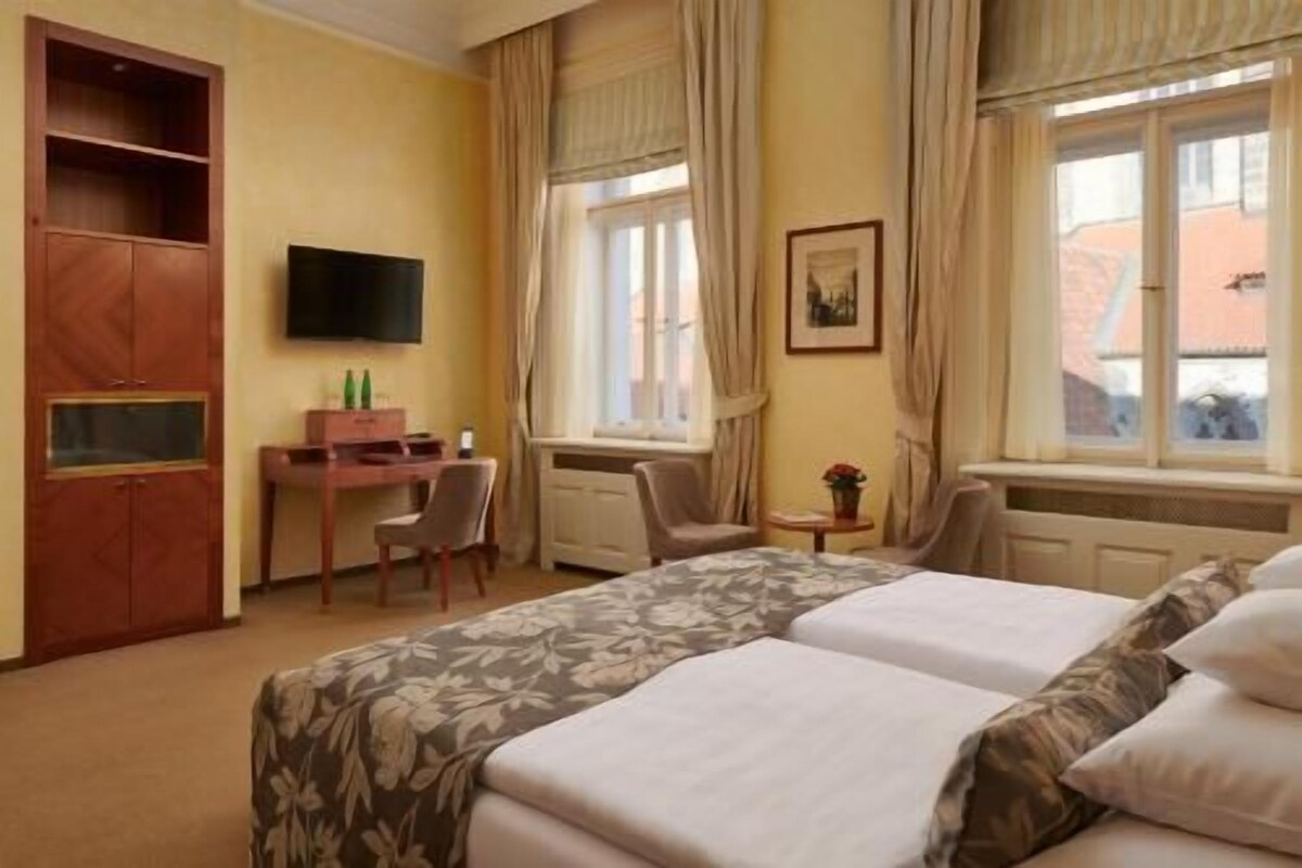 Ein Hotelzimmer mit zwei Betten, einem Schreibtisch, einem Stuhl, einem Fernseher und einem Fenster mit Vorhängen.