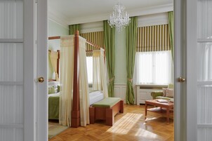 Quarto com cama de dossel, mesa de cabeceira, cadeira e janela com cortinas.
