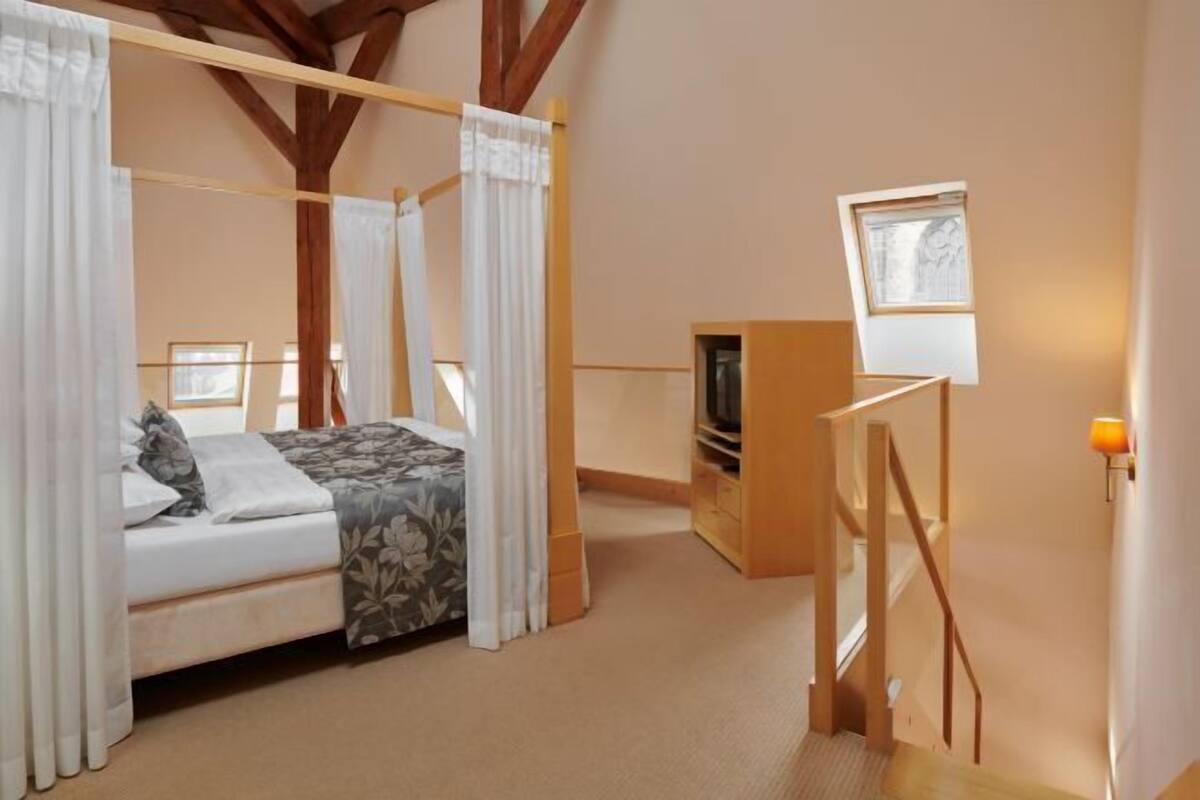 Un dormitorio con una cama con dosel, un televisor y un escritorio pequeño con una lámpara.