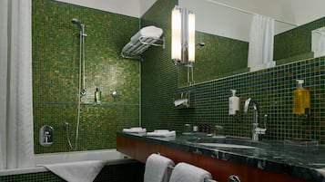 Ein Badezimmer mit grüner Mosaikfliesenwand, einer Dusche, einem Waschbecken mit Spiegel und einem Handtuchhalter.