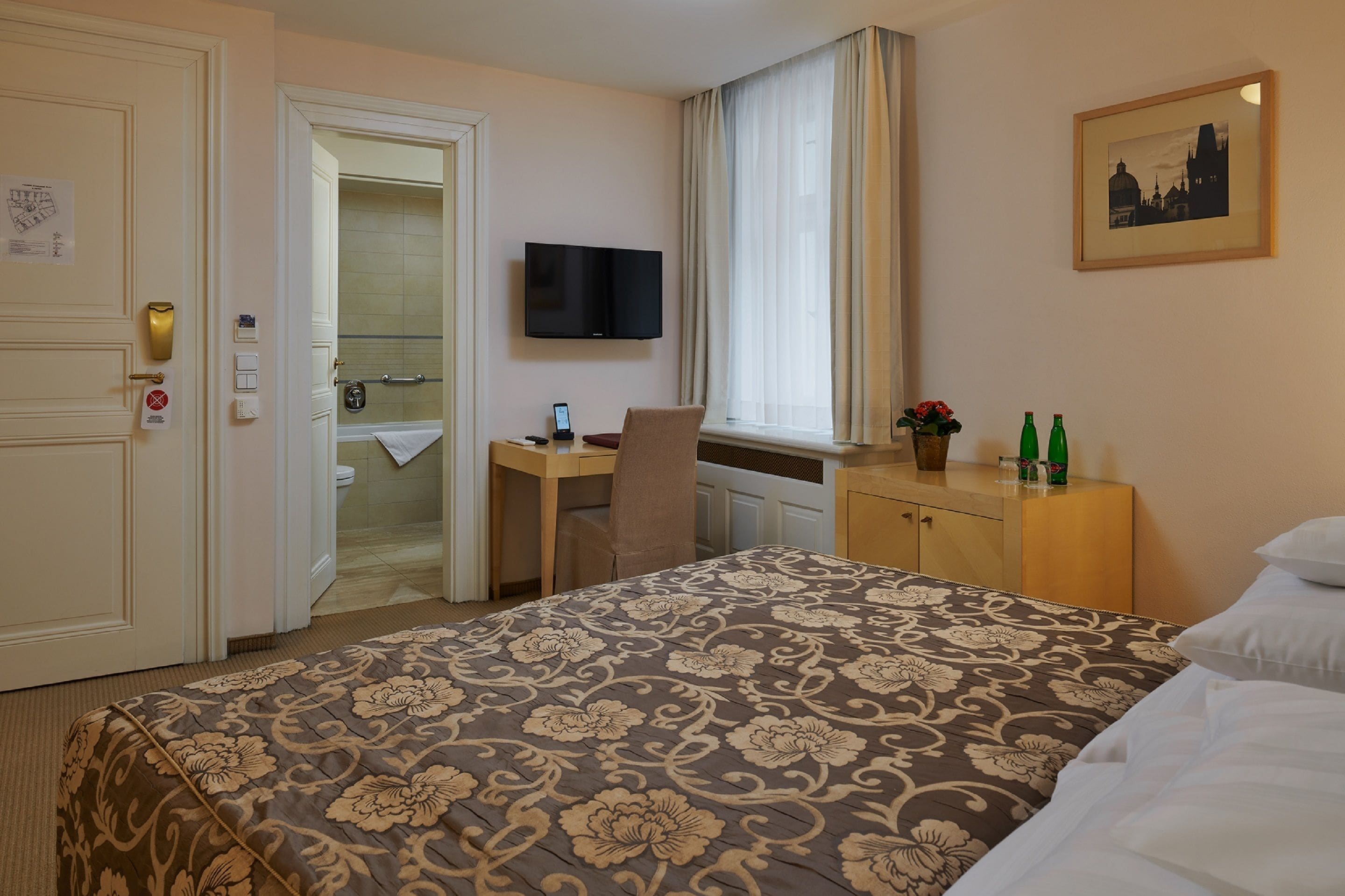A hotel room with a bed, a desk, a chair, a television, and a window with curtains.
