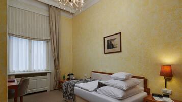 Une chambre d’hôtel avec un lit, une table de chevet, une lampe, une fenêtre avec des rideaux, un radiateur et un tableau au mur.