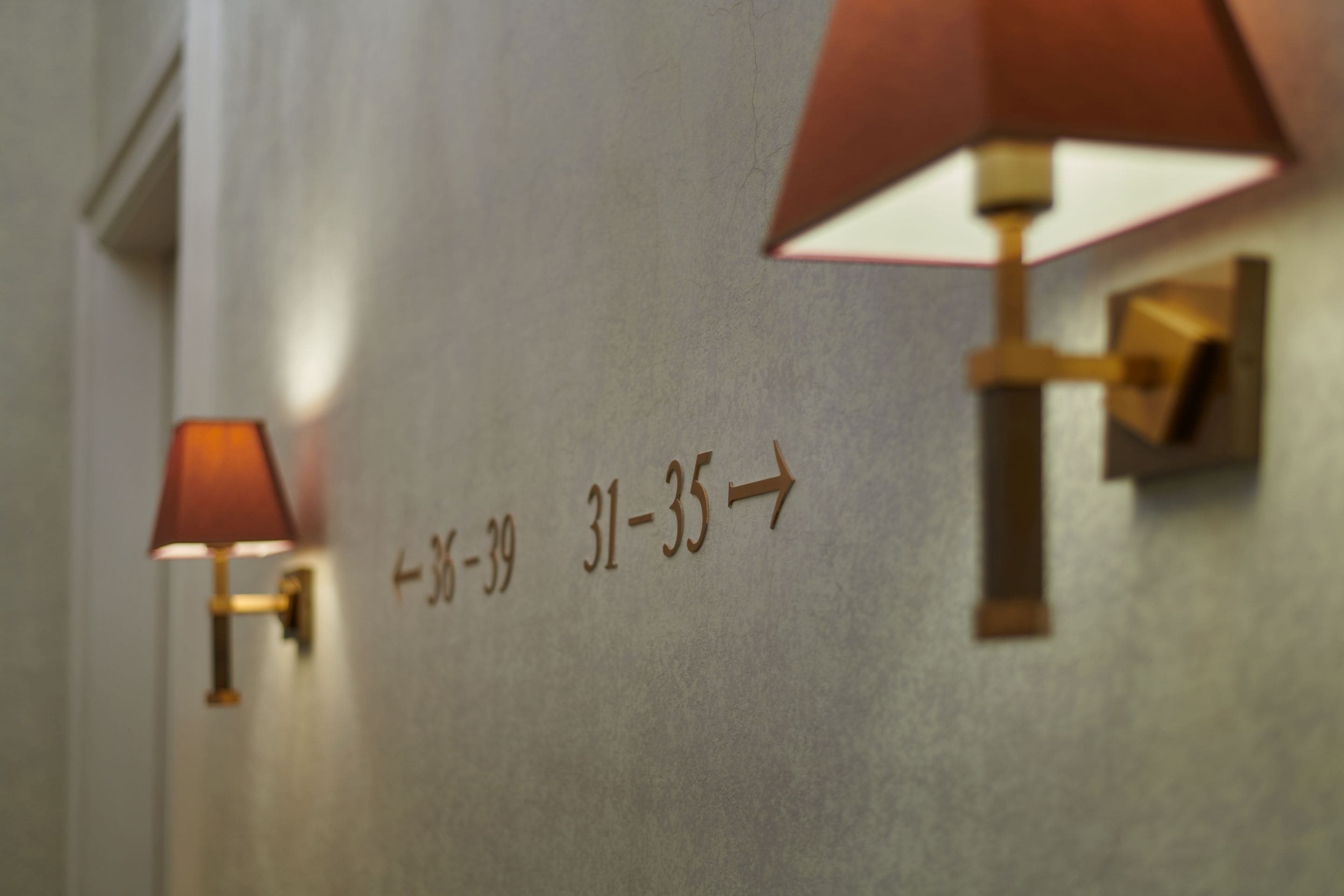 A hallway with directional signs and wall-mounted lamps.