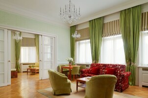 Uma sala de estar ampla com um sofá floral vermelho, poltronas verdes, uma mesa de centro de madeira e um lustre.