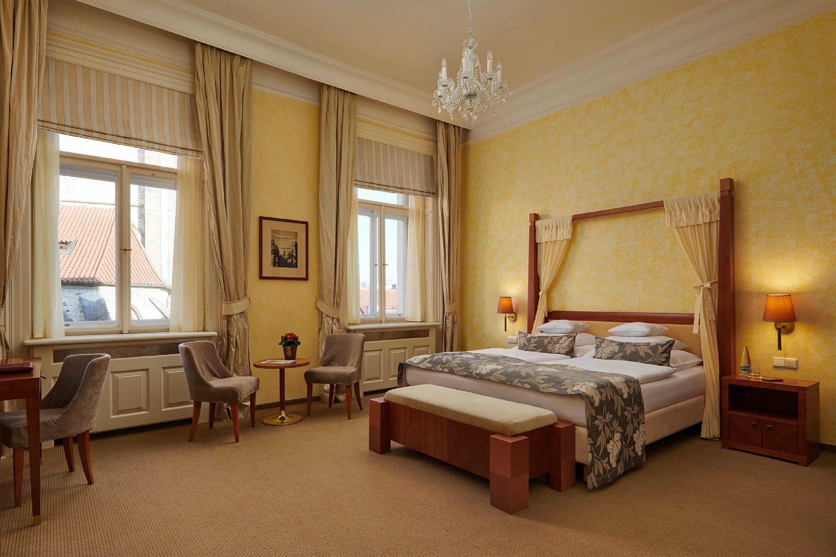 Ein Hotelzimmer mit Himmelbett, Sitzecke mit Sesseln, einem kleinen Tisch und einer Bank.