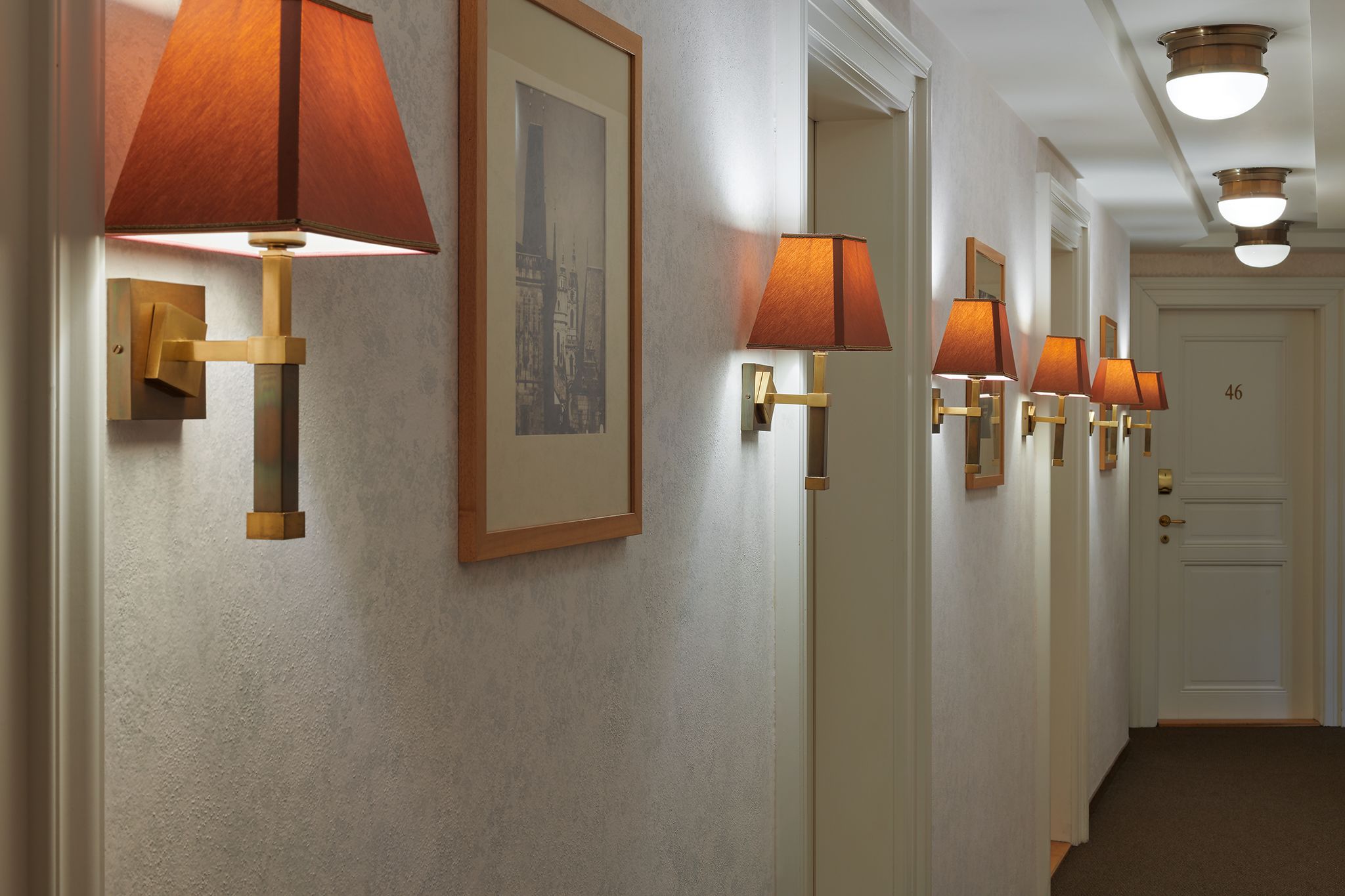 Um corredor com luminárias na parede e quadros emoldurados.