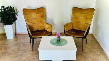 Two armchairs with a white coffee table in between, a potted plant to the left, and a white wall with a power outlet.