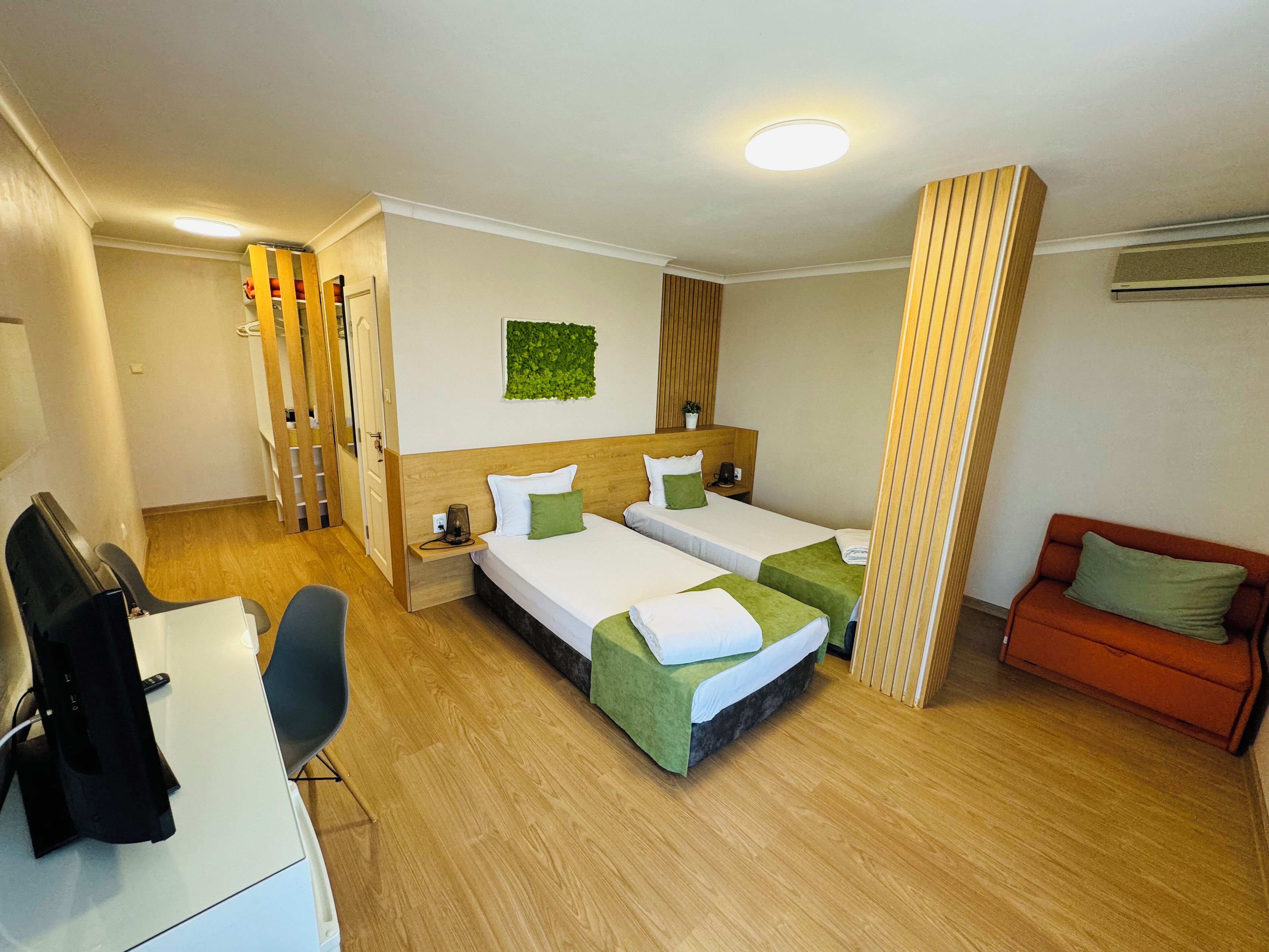 A hotel room with two beds, a desk, a chair, a small sofa, and a TV.