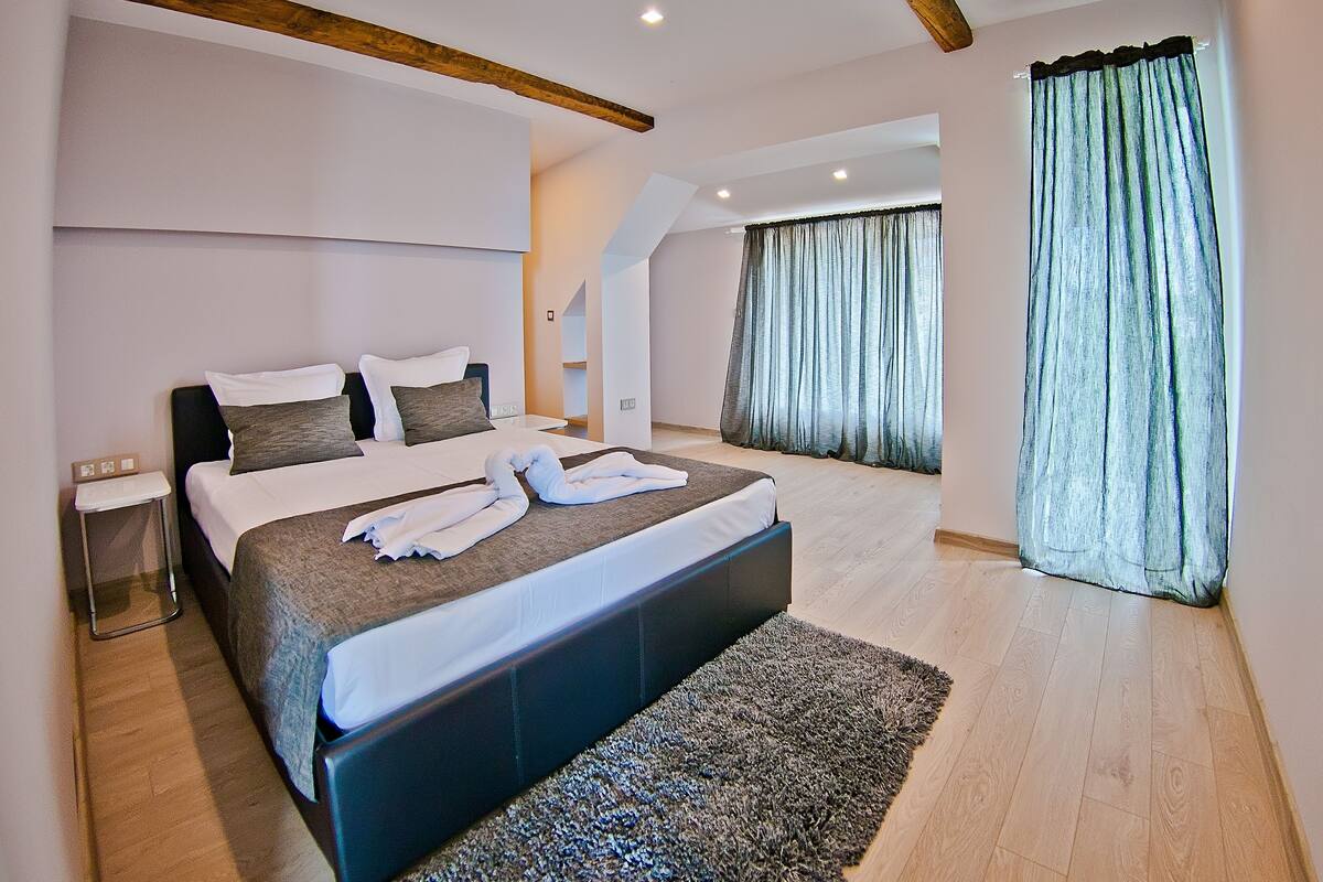 A modern bedroom with a large bed, a bedside table, and a view of a balcony.