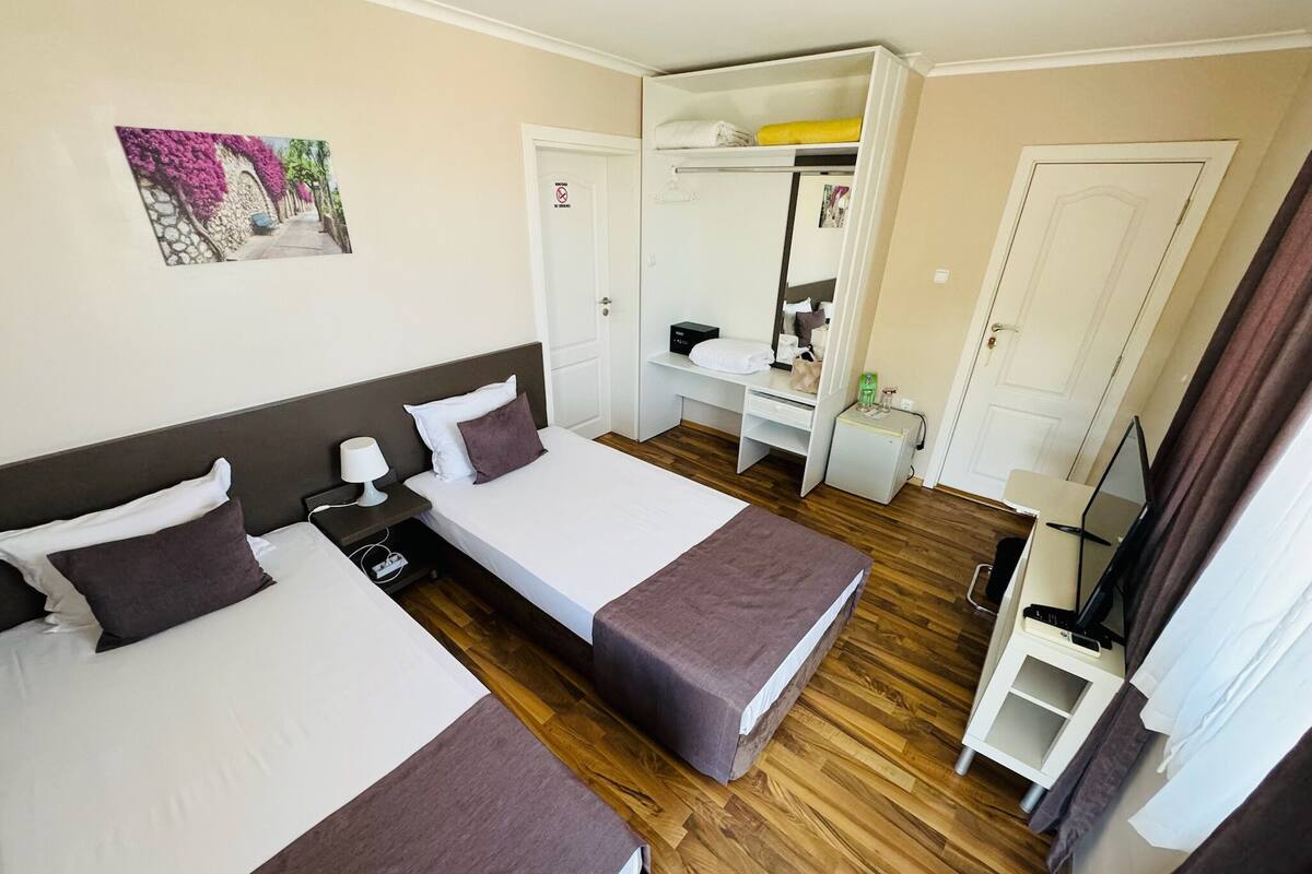 A hotel room with two beds, a desk, a wardrobe, and a mirror.