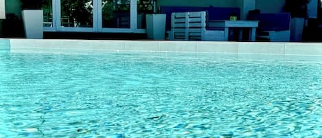 A swimming pool with clear water, surrounded by a building with large windows and potted plants.