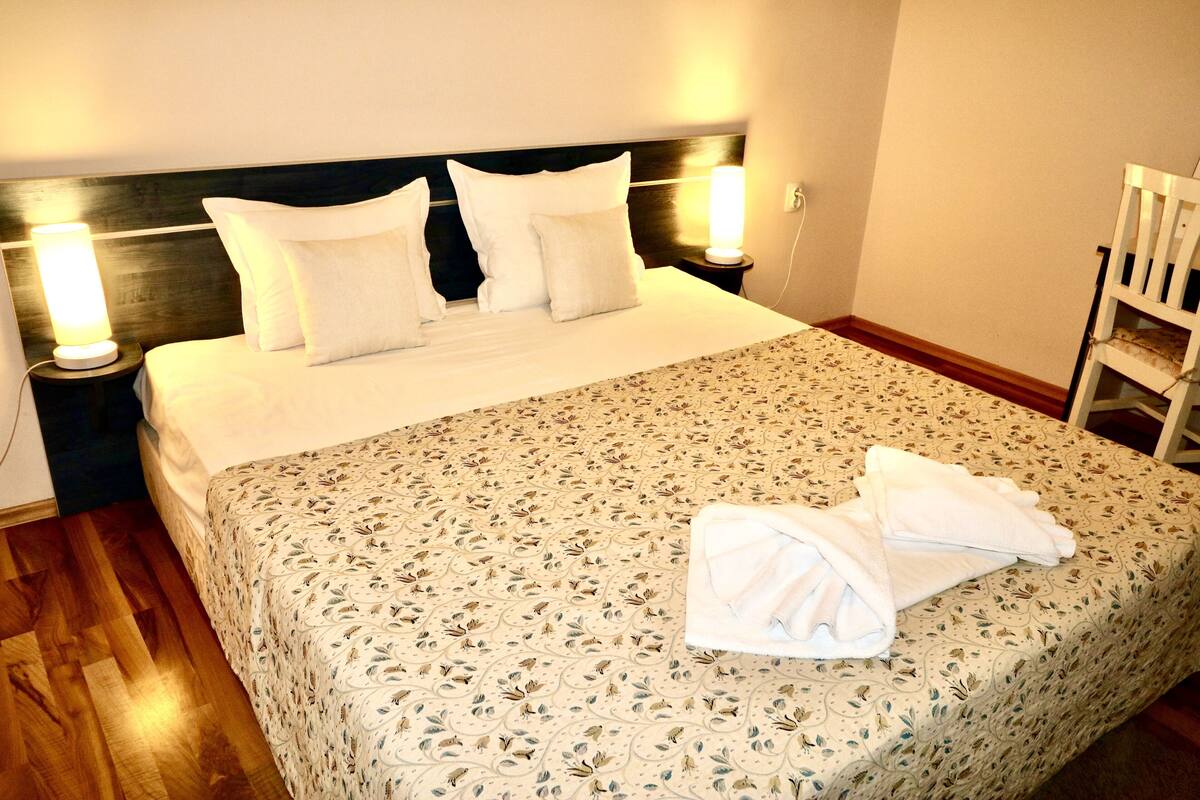 A neatly made bed with a floral bedspread, two bedside lamps, and a chair in a hotel room.
