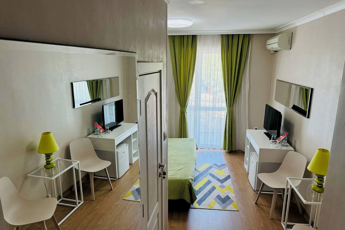 A hotel room with a bed, two desks with computers, a TV, and a mirror.