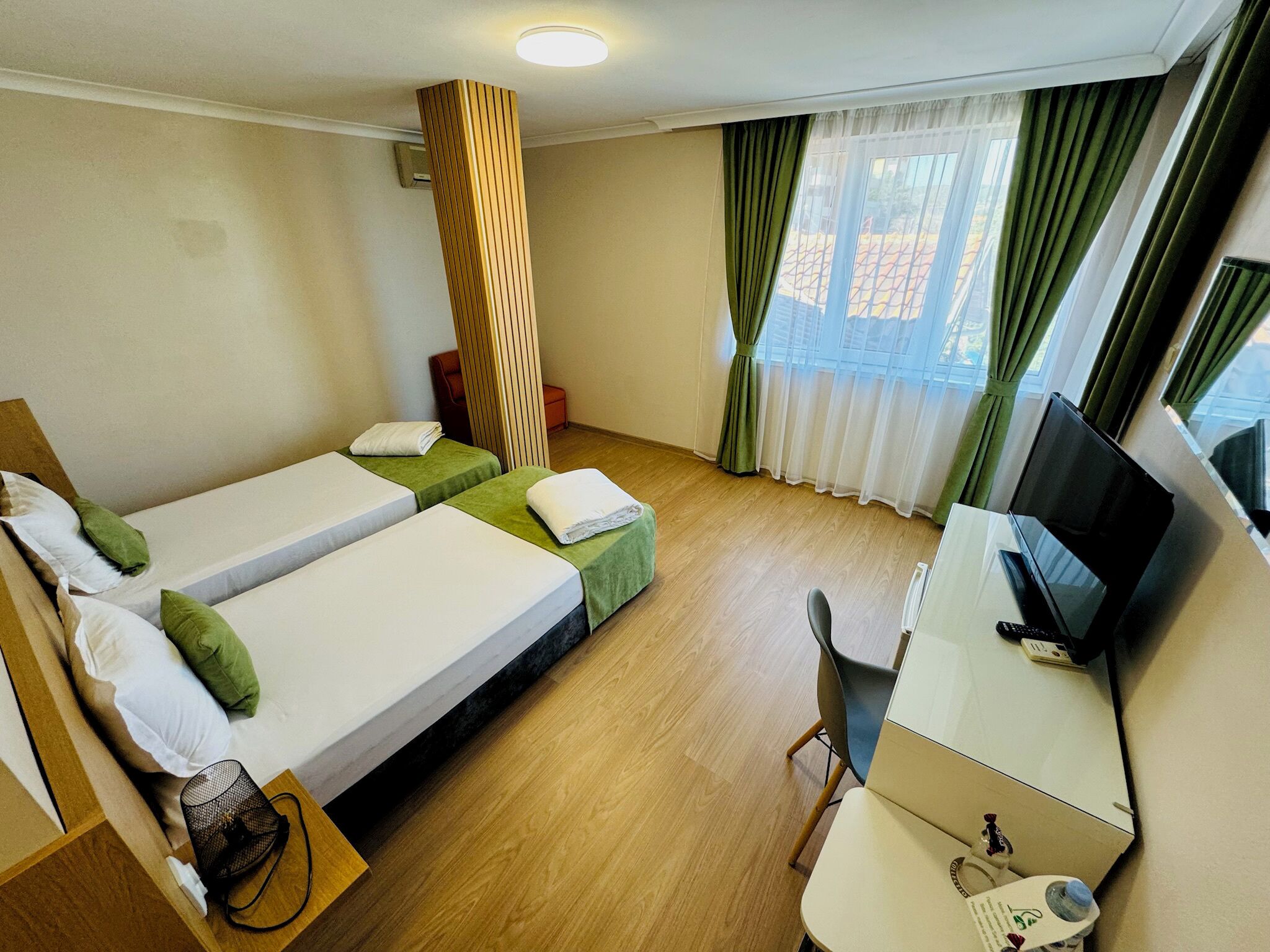 A hotel room with two beds, a desk, a TV, and a window with curtains.