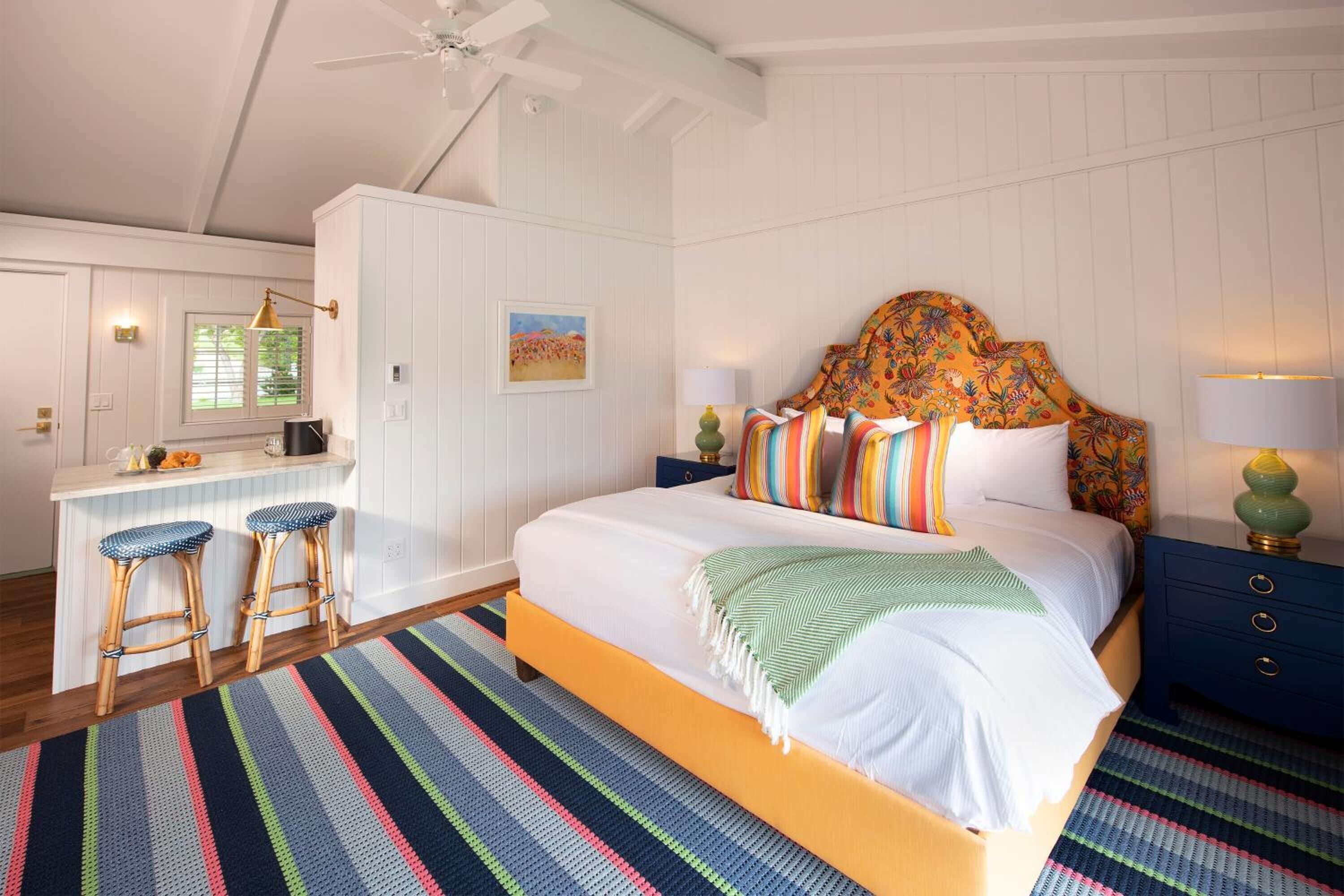 A bedroom with a bed, a desk, and two stools.