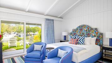 Een slaapkamer met een bed, twee blauwe fauteuils, een nachtkastje, een lamp en uitzicht op boten door een schuifglazen deur.