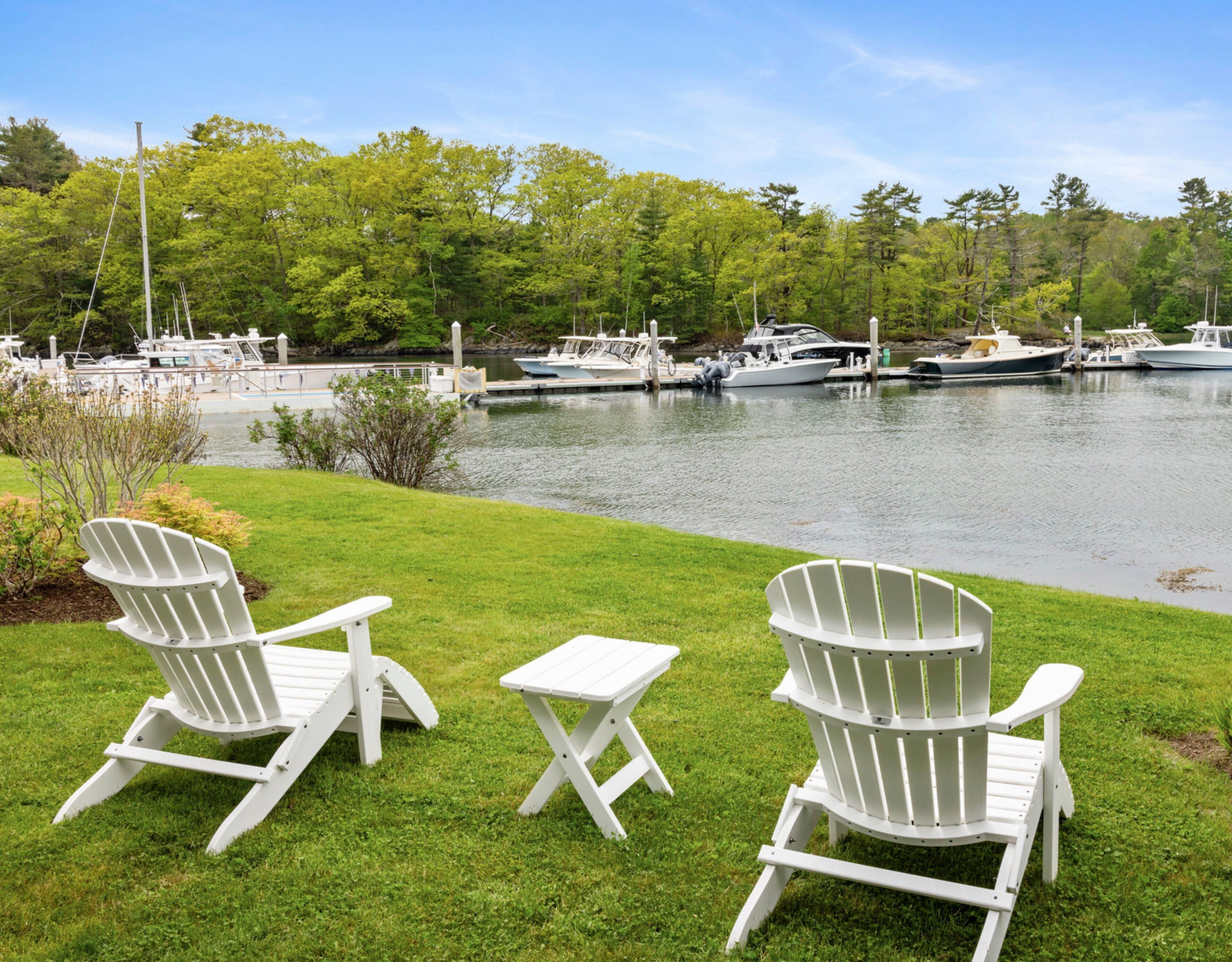 Two Adirondack chairs on a grassy lawn with a marina and boats in the background.