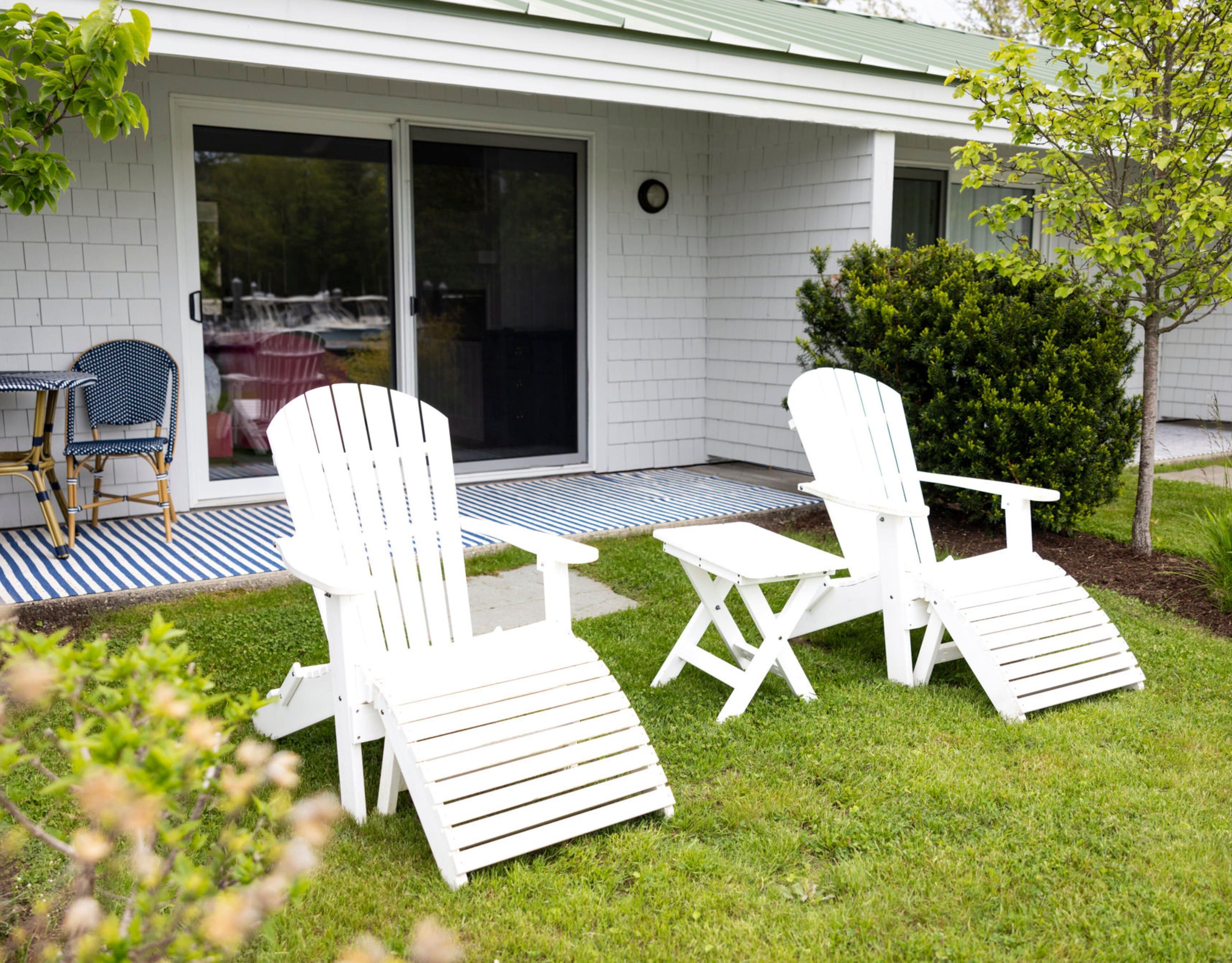 A patio with two white Adirondack chairs, a small table, and a blue and white striped rug.